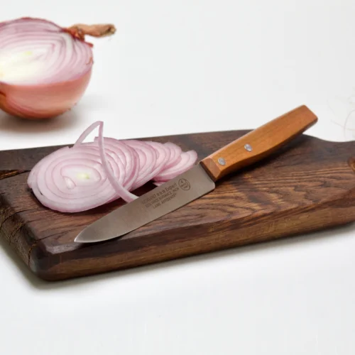 couteau microdentée sur une planche en bois et un oignon rose découpé finement